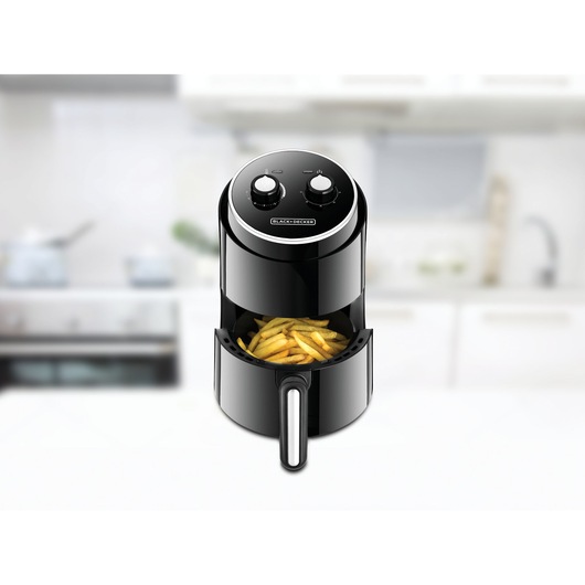 Photo of BLACK+DECKER AF100 black air fryer with fries in basket, front view, kitchen background.