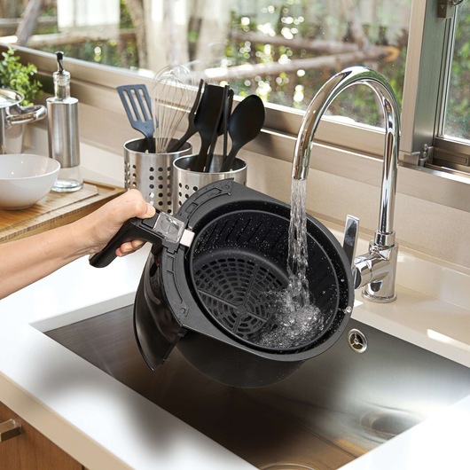 BLACKDECKER AF100 air fryer basket being rinsed under faucet in modern kitchen sink.