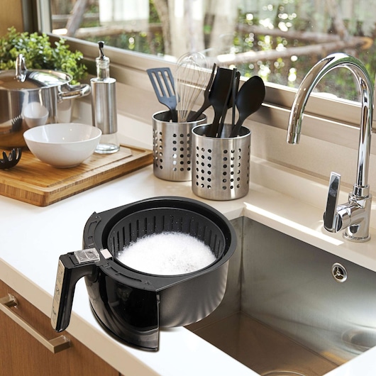 BLACKDECKER AF250G air fryer basket with soap suds placed in a kitchen sink, surrounded by utensils and cookware.