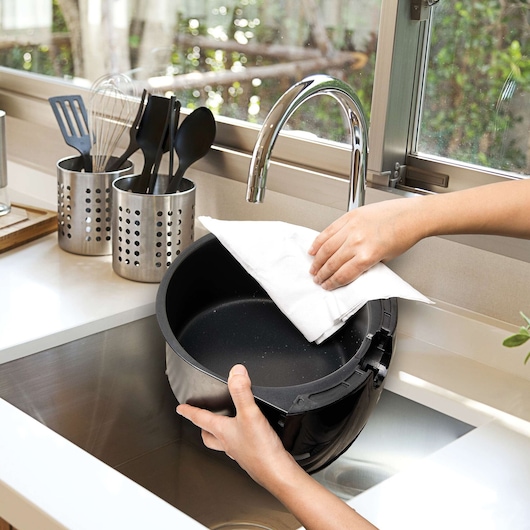 BLACKDECKER AF250G bowl being cleaned by hand in kitchen sink, utensils visible in background.