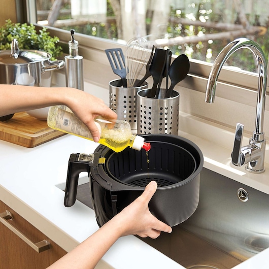 BLACKDECKER AF400 air fryer basket held over kitchen sink with oil being poured, side angle.