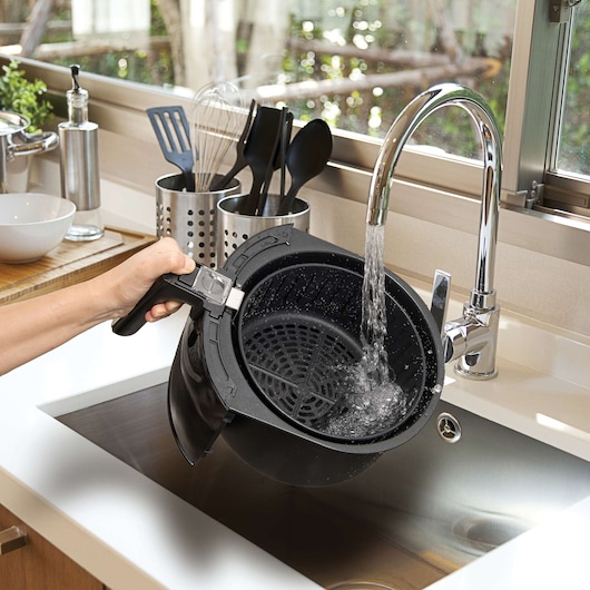 BLACKDECKER AF400 air fryer basket being washed under a kitchen faucet in a modern kitchen sink.