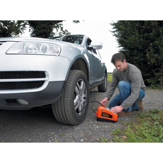 BLACKDECKER ASI300 portable air compressor inflating car tire outdoors.
