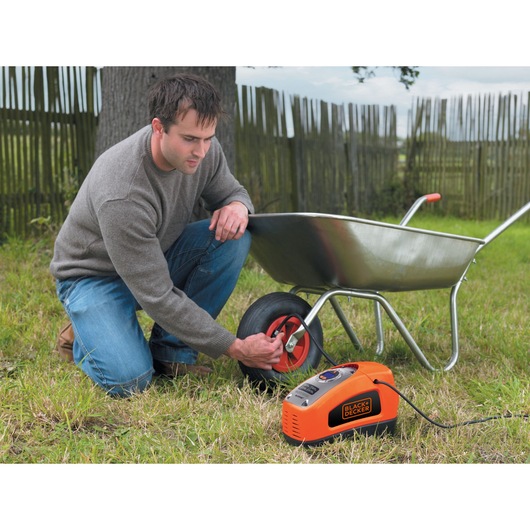 Photo of BLACKDECKER ASI300 portable air compressor inflating a wheelbarrow tire outdoors.