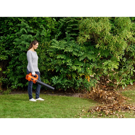 BLACKDECKER BCBL200B cordless leaf blower in use blowing leaves on grass in a garden.