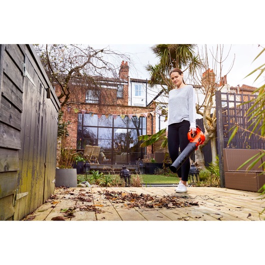BLACKDECKER BCBL200B leaf blower held outdoors, clearing leaves from wooden patio, garden background.