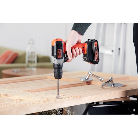 Photo of BLACK+DECKER cordless drill BCD001C2K in use on wood, close-up, with wood shavings visible.