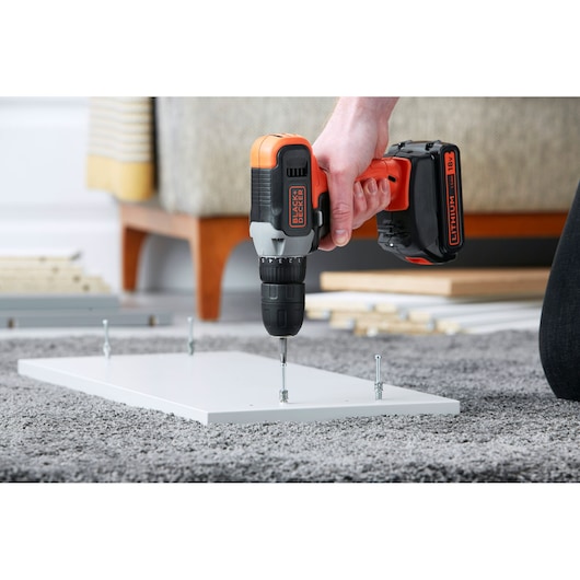 BLACK+DECKER BCD001C2K cordless drill in use assembling furniture, close-up on carpeted floor.