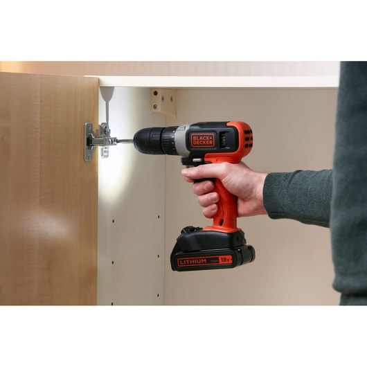 BLACK+DECKER BCD001C2K cordless drill in use installing a cabinet hinge, side view, orange and black color.