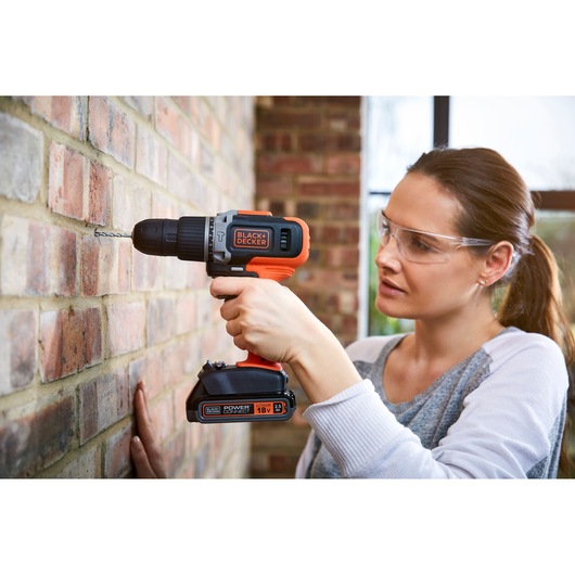 Photo of BLACK+DECKER cordless drill BCD003C1 in use drilling into a brick wall, close-up view.