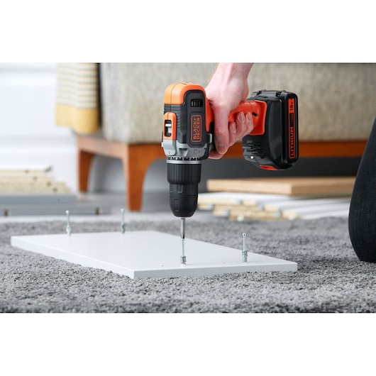 BLACKDECKER BCD003C2K cordless drill driving screw into white board on carpet during assembly.