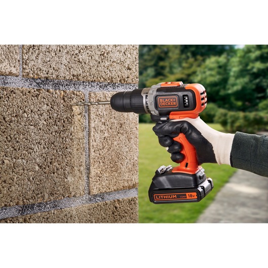 BLACKDECKER BCD003C2K cordless drill in use drilling into a brick wall outdoors.