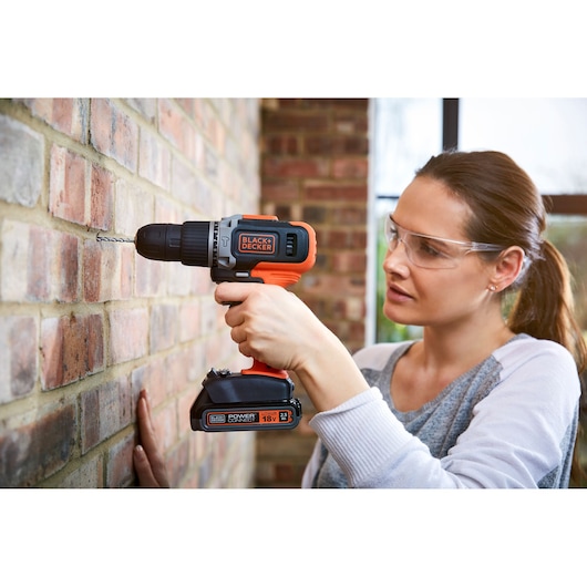 BLACK+DECKER BCD003C2K cordless drill in use on brick wall, shown closeup from the side.
