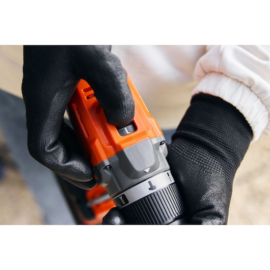 Close-up photo of BLACKDECKER BCD383D1 drill with hand adjusting settings, orange and gray body.