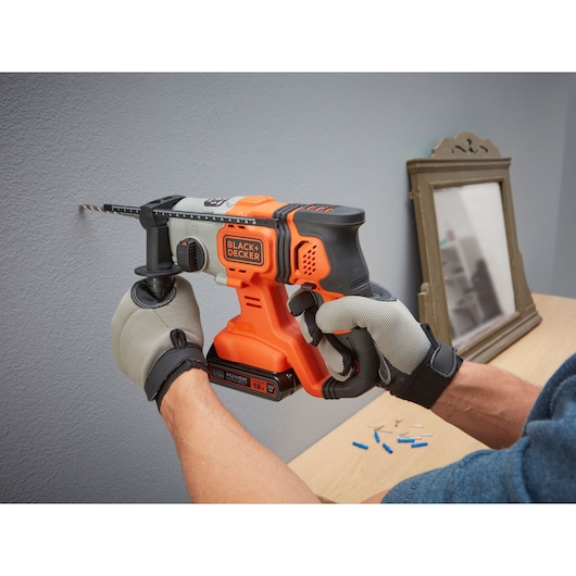 BLACK+DECKER BCD900B cordless hammer drill in use on a wall, close-up side view, operator wearing gloves.