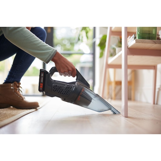BLACKDECKER BCHV001C1 handheld vacuum being used to clean debris from wooden floor near furniture.