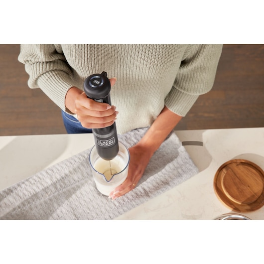 BLACK+DECKER BCKM101MFFF hand blender mixing milk in glass measuring cup on kitchen counter.