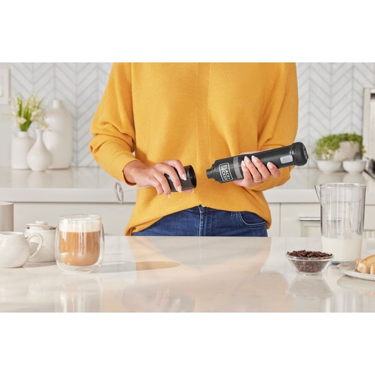 Photo of BLACK+DECKER BCKM101MFFF handheld milk frother in kitchen setting, held by person in yellow sweater.