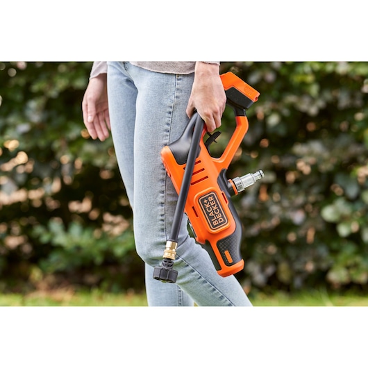Photo of a person holding a BLACK+DECKER BCPC18D1 cordless pressure washer outdoors.