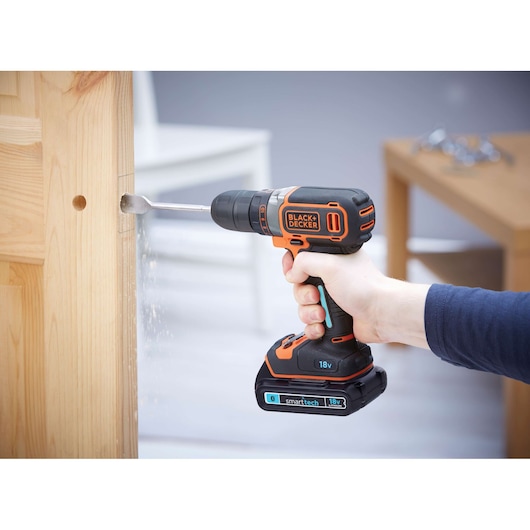 BLACKDECKER BDCDC18KST cordless drill in use drilling wood, black and orange design, photography close-up.