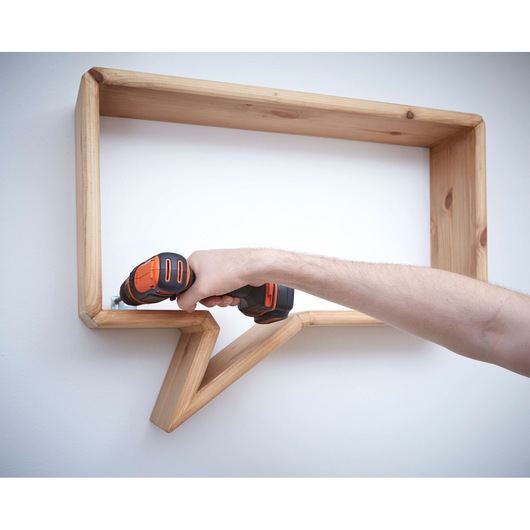 BLACKDECKER BDCDD12 cordless drill used to mount a wooden shelf on a wall.