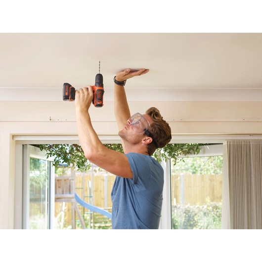 Photo of a person using BLACK+DECKER BDCDD12 cordless drill to drill into a ceiling indoors.