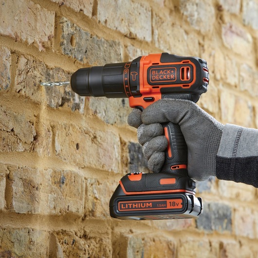 Photo of BLACK+DECKER BDCHD18KB cordless drill being used to drill into a brick wall, shown in a gloved hand.