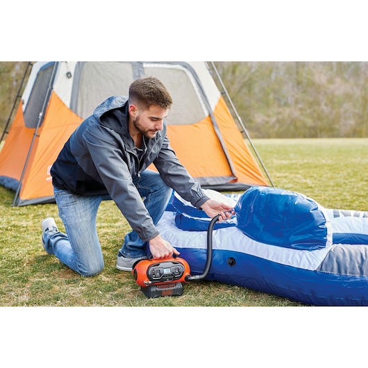 BLACKDECKER BDCINF18N inflator used to inflate an air mattress outdoors near an orange tent.