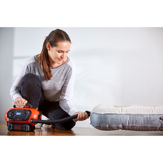 BLACKDECKER BDCINF18N air inflator used to inflate a mattress indoors, product in use with hose attached.