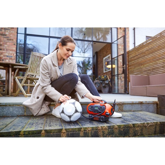 BLACKDECKER BDCINF18N orange portable inflator in use to inflate a white soccer ball outdoors.