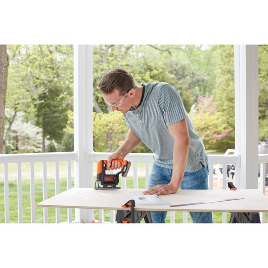 BLACKDECKER BDCK502C1 cordless jigsaw in use cutting wood outdoors on a sawhorse worktable.