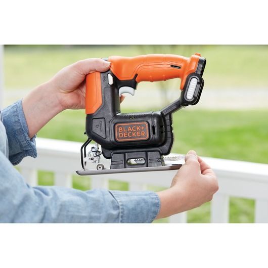 Photo of BLACK+DECKER BDCK502C1 cordless jigsaw in use, showing black and orange handle and visible blade.
