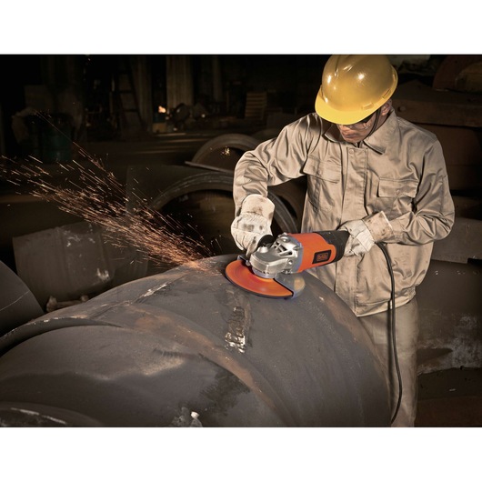 Worker using BLACKDECKER BDGL2218 angle grinder on large metal pipe, sparks flying, wearing safety gear.