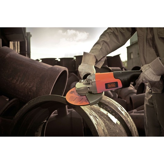 Photo of BLACK+DECKER BDGL2218 angle grinder in use on a metal pipe outdoors, operator wearing gloves.
