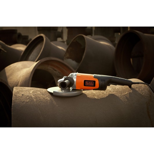BLACK+DECKER BDGL2218 angle grinder with orange and black body on large metal pipe, side view.