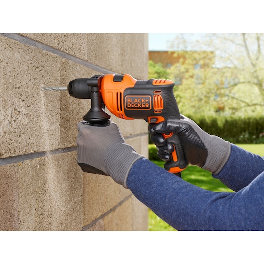 BLACK+DECKER BEH550 corded drill in use drilling into a concrete wall outdoors.