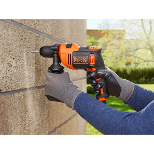 BLACKDECKER BEH710K orange cordless drill in use on concrete wall outdoors, close-up view.