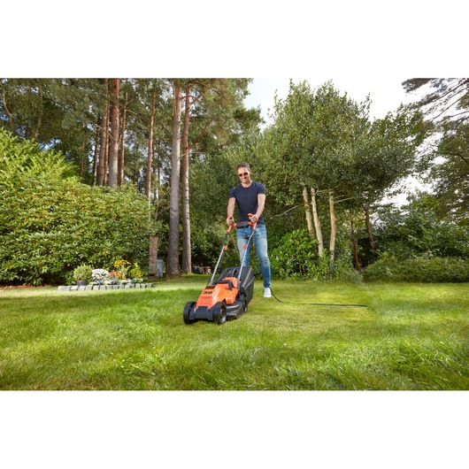 BLACKDECKER BEMW451BH lawn mower in use on grass outdoors, orange and black design, garden background.