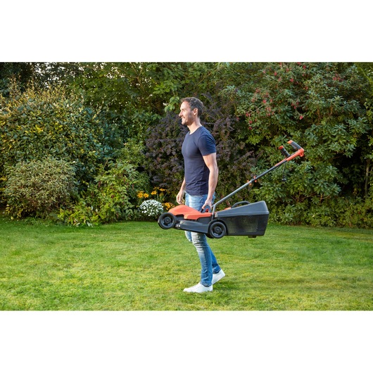 BLACK+DECKER BEMW451BH lawn mower being carried by a person in a garden, orange and black color.