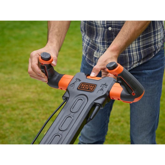 Photo of BLACKDECKER BEMW481ES lawn mower handle with ergonomic orange and black controls in use outdoors.