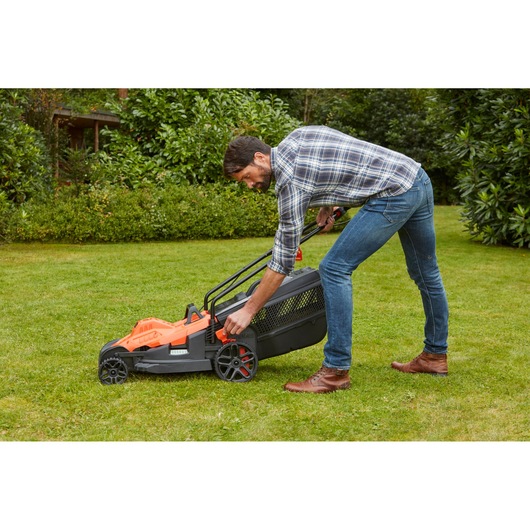 Person adjusting BLACKDECKER BEMW481ES electric lawn mower height lever on grass in a garden.