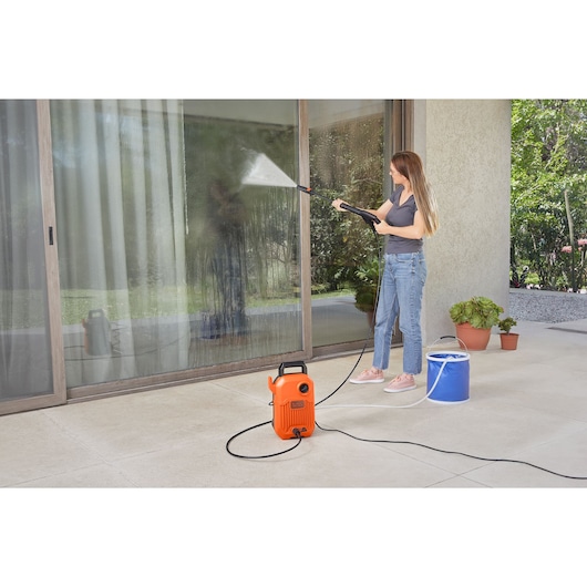 BLACKDECKER BEPW1300 pressure washer in use, cleaning glass doors outdoors, orange unit with hose and spray wand.