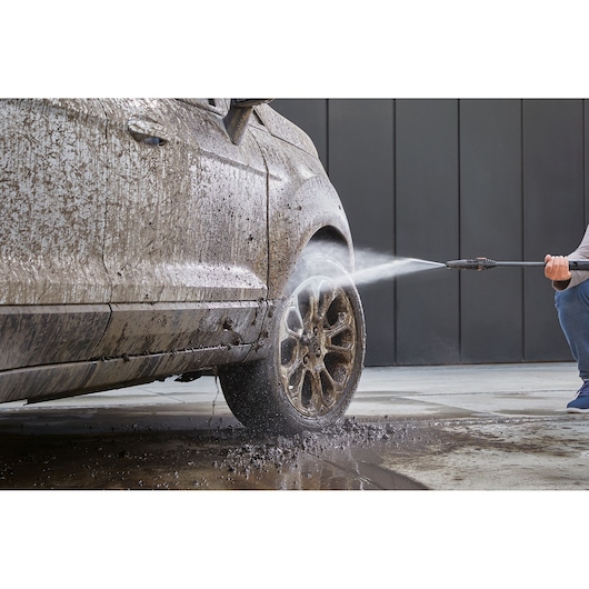 BLACKDECKER BEPW2000 pressure washer cleaning muddy car wheel, photo shows water spray removing dirt.