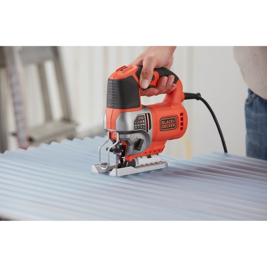 Photo of BLACKDECKER BES610 jigsaw cutting corrugated sheet, orange and black design, handheld power tool.