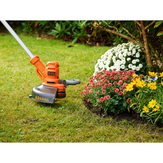 BLACKDECKER BESTA530CM grass trimmer in use near flower beds on lawn, side angle photo.