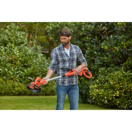 BLACKDECKER BESTA530CM orange grass trimmer held outdoors by person wearing plaid shirt.