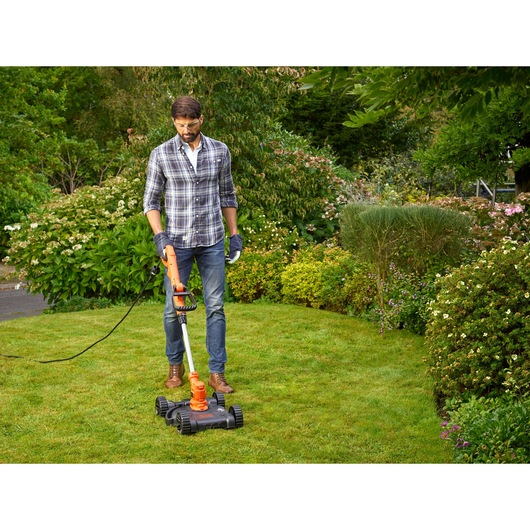 BLACKDECKER BESTA530CM corded lawn mower in use on green grass in garden setting.