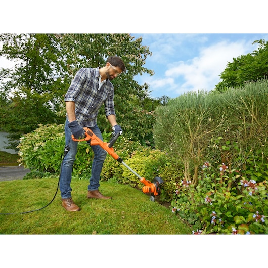 Photo of a person using a BLACKDECKER BESTA530 electric grass trimmer on lawn edge in a garden.