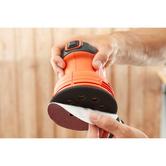 Photo of BLACKDECKER BEW210 random orbital sander with sandpaper disc being attached, close-up view.