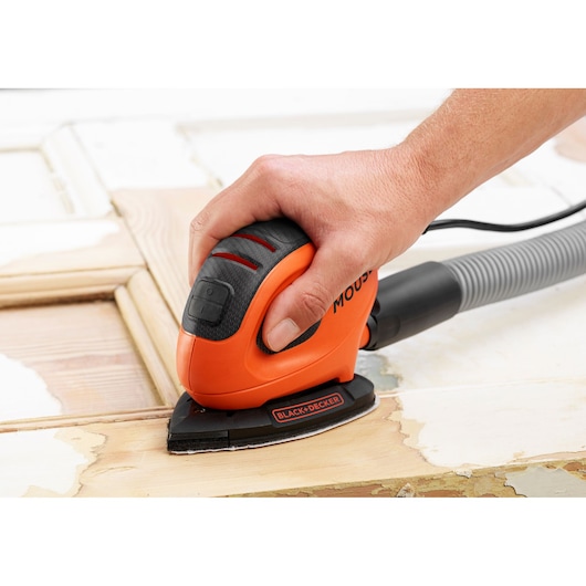 Photo of BLACK+DECKER BEW230 detail sander in use on wooden surface, showing ergonomic grip and dust extraction hose.